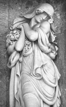Statue of a classical woman with roses regretting the loss of a beloved one in the cemetery