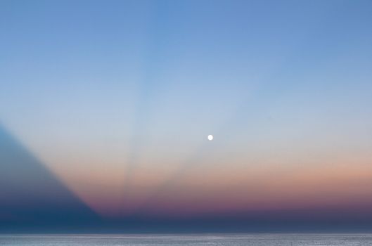 Abstract and dramatic sunset with light rays that create the shape of an inverted pyramid on the sea.