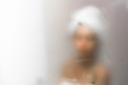 Young woman reflected in the mirror blurred by the steam. Defocused blurry background.