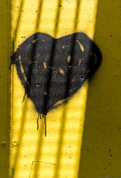 Dark heart painted on wall with spray paint. The shadows created by the sun's rays make it look like behind the bars of a prison.
