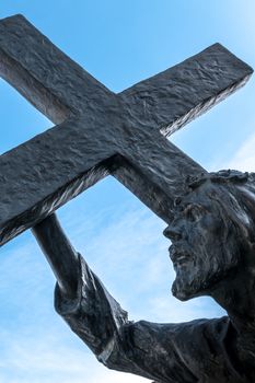 Bronze statue of Jesus carrying his cross, on the way to his crucifixion. Ideal for the easter concept, resurrection and other. Blue sky with white clouds on background.