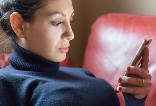 Young caucasian woman using her smartphone on red couch at home in the living room. Ideal for concepts.