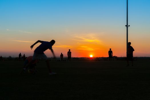 Young unrecognisable males practicing and training at soccer silhouetted at twilight