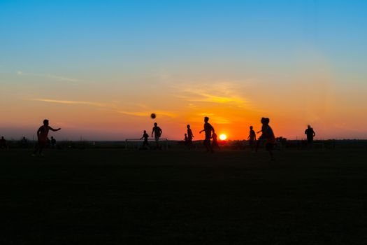 Young unrecognisable males practicing and training at soccer silhouetted at twilight