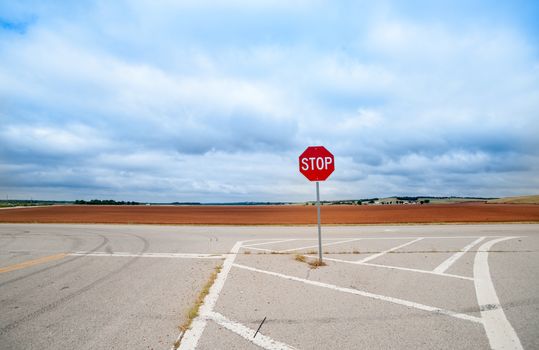 Rich red soil and agricultural land from Route 66 behind red stop sign in middle of intersection, Oklahoma on Route 66