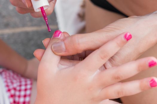 Woman applying nail polish, doing manicure to a little girl, fun activity at home, girl birthday party, spring and summertime.