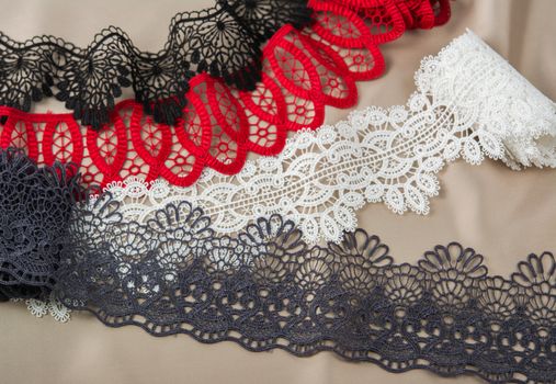 pile of red, white. black and gray gentle luxury quality guipure, lace fabric on beige background. use for sew clothes linen decoration. texture for websites