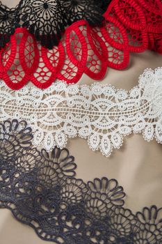 pile of red, white. black and gray gentle luxury quality guipure, lace fabric on beige background. use for sew clothes linen decoration. texture for websites