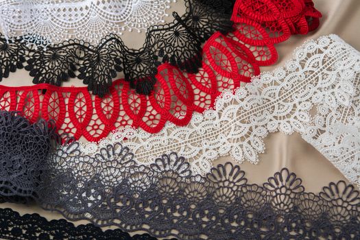 pile of red, white. black and gray gentle luxury quality guipure, lace fabric on beige background. use for sew clothes linen decoration. texture for websites