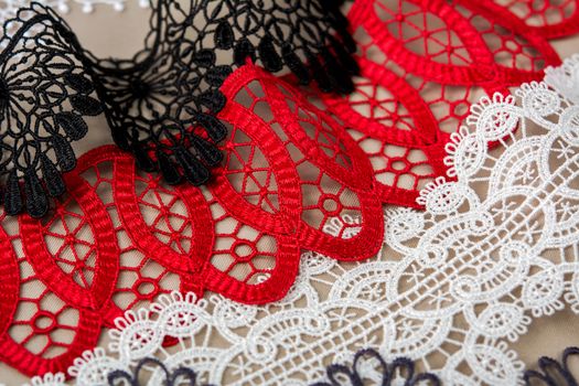 pile of red, white. black and gray gentle luxury quality guipure, lace fabric on beige background. use for sew clothes linen decoration. texture for websites