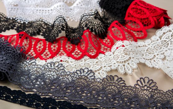 pile of red, white. black and gray gentle luxury quality guipure, lace fabric on beige background. use for sew clothes linen decoration. texture for websites