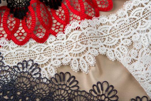 pile of red, white. black and gray gentle luxury quality guipure, lace fabric on beige background. use for sew clothes linen decoration. texture for websites