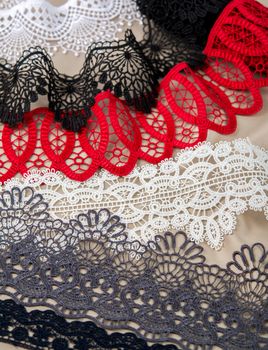 pile of red, white. black and gray gentle luxury quality guipure, lace fabric on beige background. use for sew clothes linen decoration. texture for websites