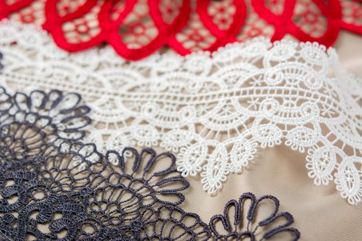 pile of red, white. black and gray gentle luxury quality guipure, lace fabric on beige background. use for sew clothes linen decoration. texture for websites