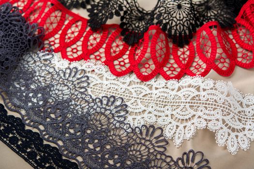pile of red, white. black and gray gentle luxury quality guipure, lace fabric on beige background. use for sew clothes linen decoration. texture for websites
