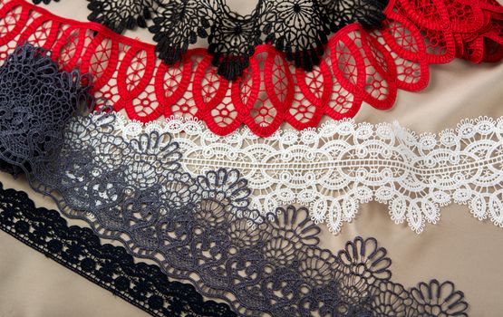 pile of red, white. black and gray gentle luxury quality guipure, lace fabric on beige background. use for sew clothes linen decoration. texture for websites