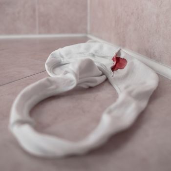 White panties in bloody stain. Beginning of the menstrual cycle. Signal of the transition from girl to woman. Selective focus.