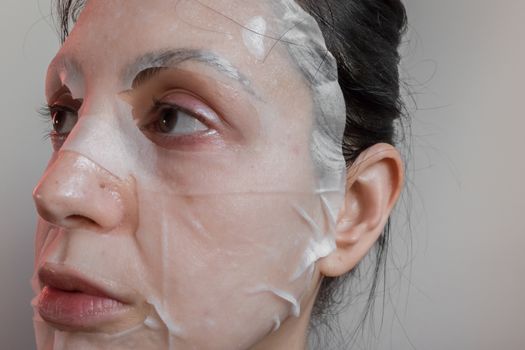Woman with a face mask sheet white. Beauty, youth, skin care.