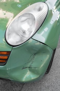 Rusty dent on front of green car, following an accident. Close-up.