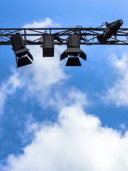 Spotlights for outdoor stage on the metal construction against a blue sky and clouds. Space for text.