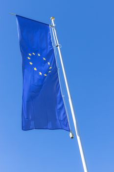 Flag of the European Union waving in the wind on flagpole against the blue sky.