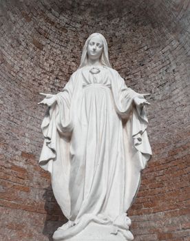 Statue in stone of Virgin Mary. On background, red brick wall. Ideal for christmas and easter concepts and other.