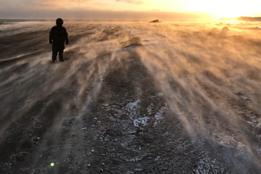 A man stands in the wind in the tundra in winter. The ground from the strong wind, the frost on the street.