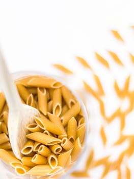 Close up of whole pasta in a glass bowl and wooden spoon on white background. Copy space.