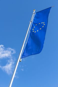 Flag of the European Union waving in the wind on flagpole against the blue sky with white cloud.