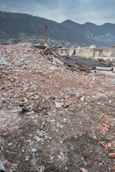 Demolition of buildings in urban environments. On background green mountains and a cloudy sky.