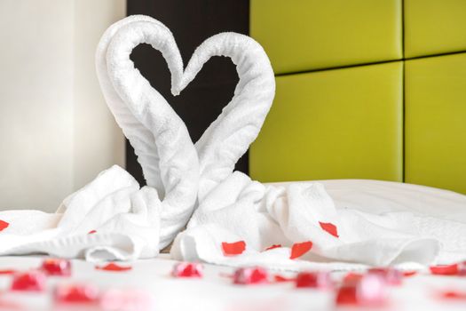 White two towel swans on the bed, sprinkled with red petals. The towel look like heart shape and it's prepare for couple in honey moon. Ideal for events and concepts.