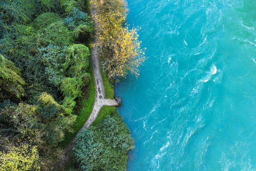 Top-down drone view of rapids of mountain river with small stone pier at the edge of the wood. Close up.