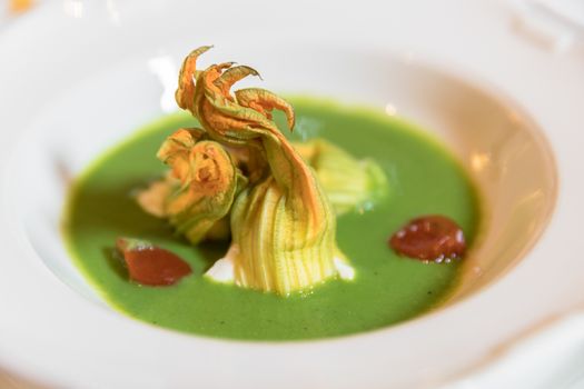 Plate of zucchini soup with pumpkin flowers and cherry tomatoes decoration. Served for wedding or event.