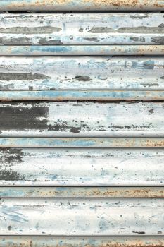 Painted metal roller shutters door with peeling paint dirty azure hue. Grungy background texture.