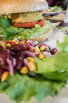 Healthy vegan burger with tomato, baked potatoes, beans, onions, salad. Close-up.