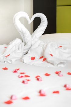 White two towel swans on the bed, sprinkled with red petals. The towel look like heart shape and it's prepare for couple in honey moon. Ideal for events and concepts.