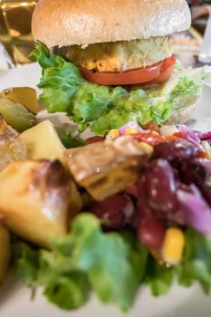 Healthy vegan burger with tomato, baked potatoes, beans, onions, salad. Close-up.