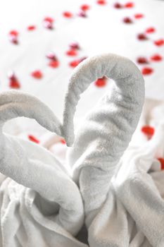 White two towel swans on the bed, sprinkled with red petals. The towel look like heart shape and it's prepare for couple in honey moon. Ideal for events and concepts.