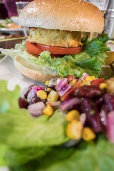 Healthy vegan burger with tomato, baked potatoes, beans, onions, salad. Close-up.