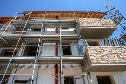 Scaffolding near a house under construction for external plaster works. Modern apartment building in city with stone balconies.