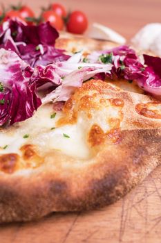 Italian pizza with chicory salad served on rustic wooden cutting board. Neapolitan crust. Selective focus. Close-up.