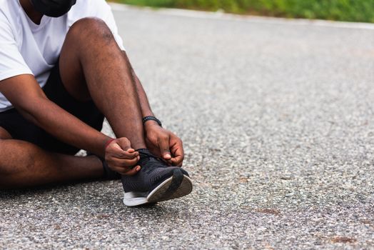 Close up Asian sport runner black man sitting shoelace trying running shoes getting ready for jogging and run at the outdoor street, health exercise workout concept