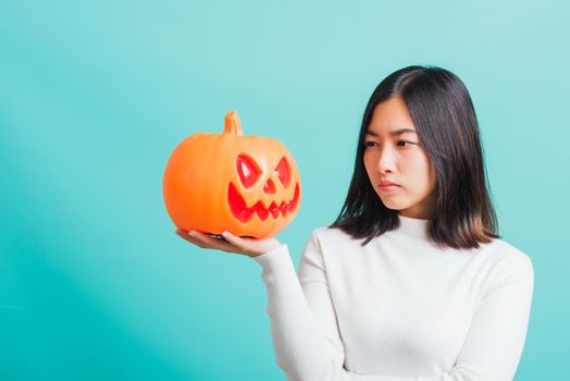 Portrait of Asian beautiful young woman holding orange model pumpkins, funny happy female with ghost pumpkins, studio shot isolated on blue background