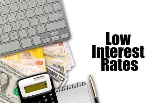 LOW INTEREST RATES text with fountain pen, keyboard, calculator, notepad and currency banknotes on white background. Business Concept