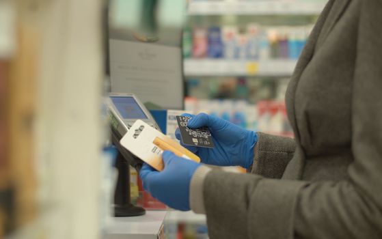 NFC technology credit card payment. Female hand in protective gloves paying with contactless credit card. Coronavirus epidemic in the city.