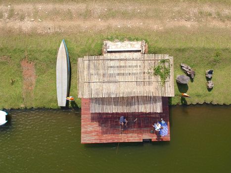 Aerial view of beautiful little wood cabana next the water of a lake, fisher on the dock of the little hut trying to catch fish. relax moment next the water in the sun.