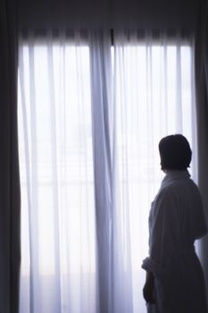 Silhouette of woman with bathrobe in front of a window. Sad atmosphere