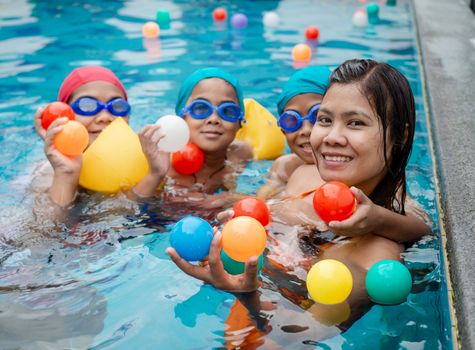 A portrait of a mother and her children playing ball in the pool.