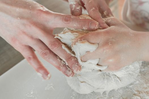 Hands of mother and daughter knead dough for pizza and bread. Having fun together in kitchen. Close-up.