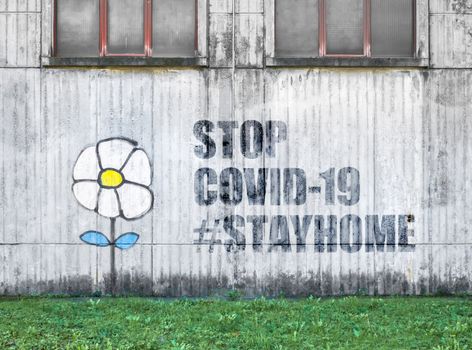 White flower painting on a facade of a factory with message STOP COVID-19 and hashtag #stayhome. COVID-19 alert concept. Lockdown. Concept of stop working activities due to coronavirus medical emergency.